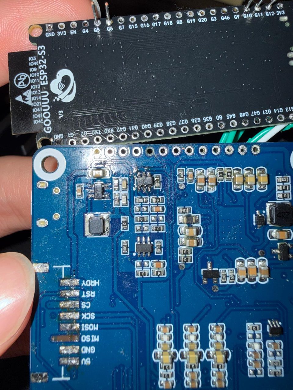 A black GOOUUU ESP32-S3 dev board lying next to the blue IT8951 driver board, with the driver's labelled SPI pads visible.
