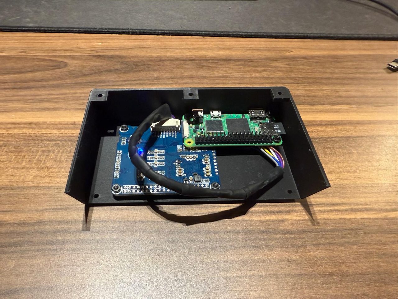 A Raspberry Pi Zero and the blue e-ink driver board wired together inside an open black 3D-printed case.